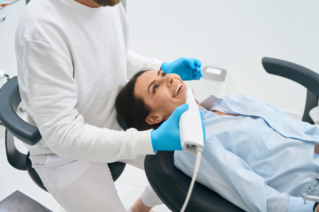 Lakeside smile Dental technician holding intraoral camera for health screening of female client, checking conditions of her oral cavity