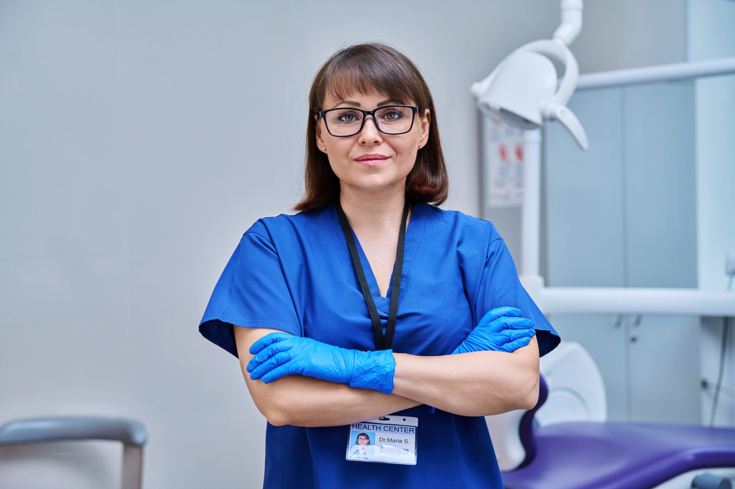 Lakeside smile female doctor dentist in office. Confident middle aged woman looking at camera with crossed arms near dental chair. Dentistry, medicine, specialist, career, dental health care concept,